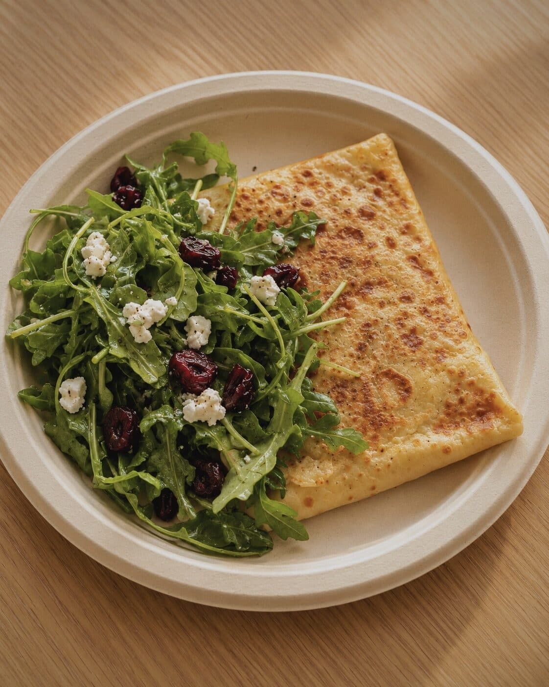 A golden savory crepe beside an arugula salad with dried cherries and goat cheese