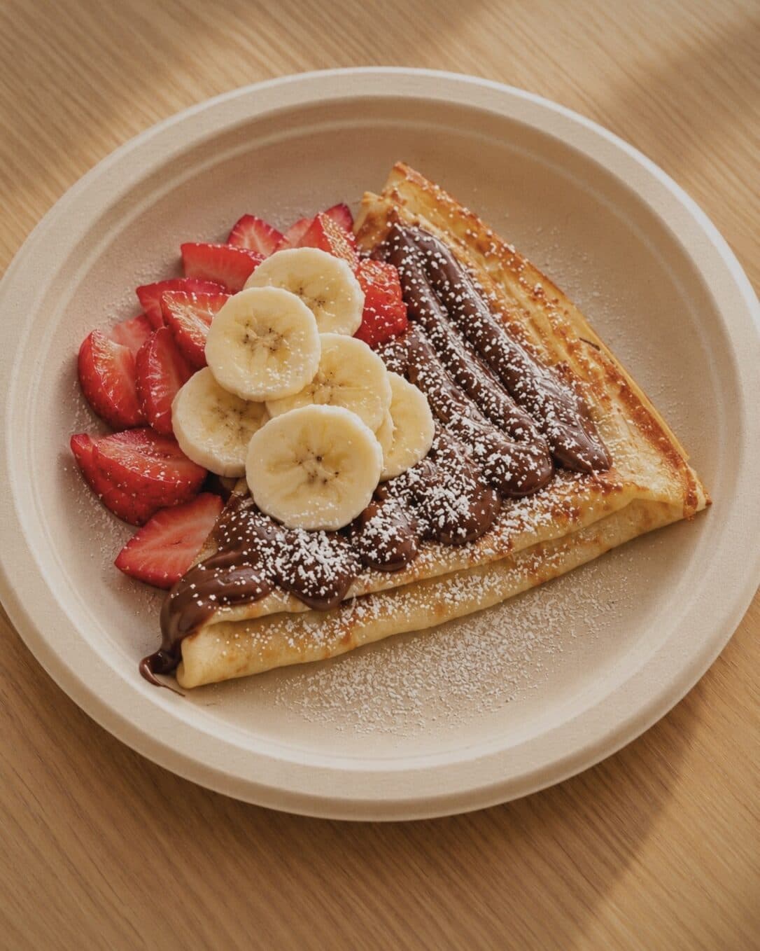 A folded crepe with chocolate hazelnut spread, banana, strawberries and powdered sugar
